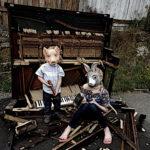 Two kids wearing animal masks with sledge hammers standing over a smashed piano.