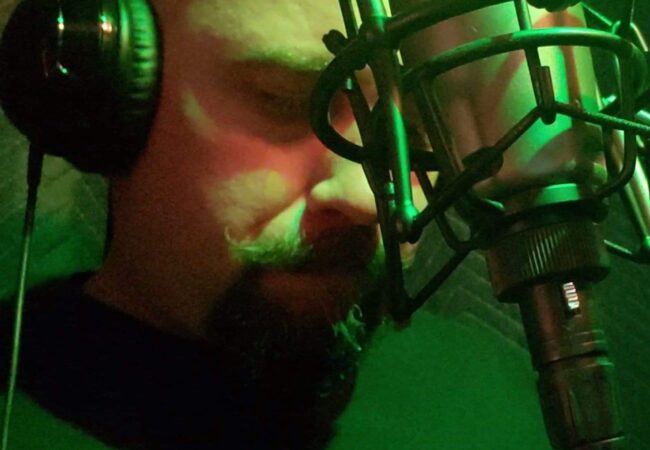 Close up of a mans face behind a microphone with headphones on.