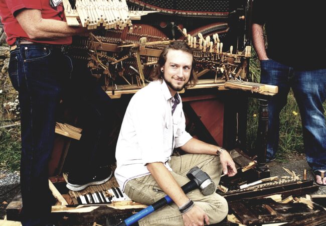 Three men standing around a smashed piano.